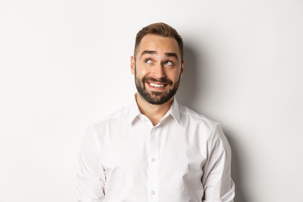 Primer plano de un hombre guapo con barba, mirando pensativo en la esquina superior izquierda, imaginando y sonriendo