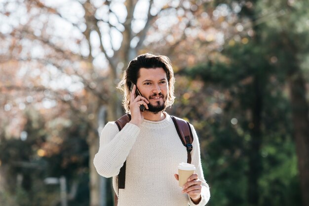 Primer plano de un hombre hablando por teléfono celular con café para llevar taza de papel