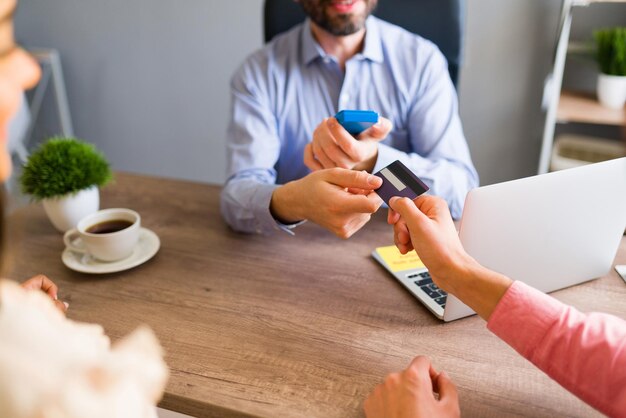 Primer plano de un hombre hispano dando su tarjeta de crédito a un representante de ventas en la agencia de viajes para pagar su viaje de negocios o vacaciones