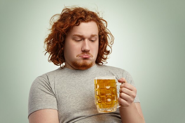 Primer plano de hombre indeciso con cabello pelirrojo sosteniendo un vaso de cerveza en sus manos