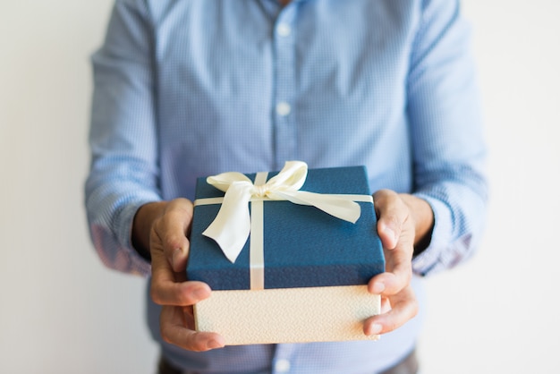 Primer plano de hombre irreconocible dando caja de regalo a la cámara