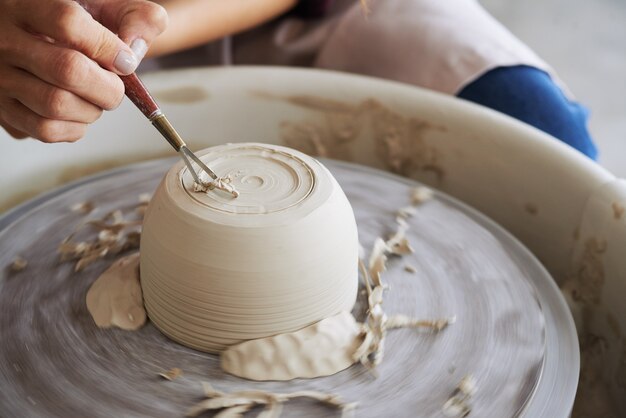 Primer plano del hombre irreconocible que talla una olla con una herramienta especial