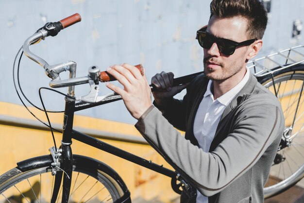 Primer plano, de, hombre joven, llevando, gafas de sol, llevar bicicleta, en su hombro