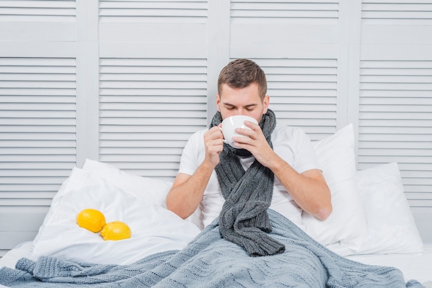 Primer plano de un hombre joven sentado en la cama bebiendo la taza de café