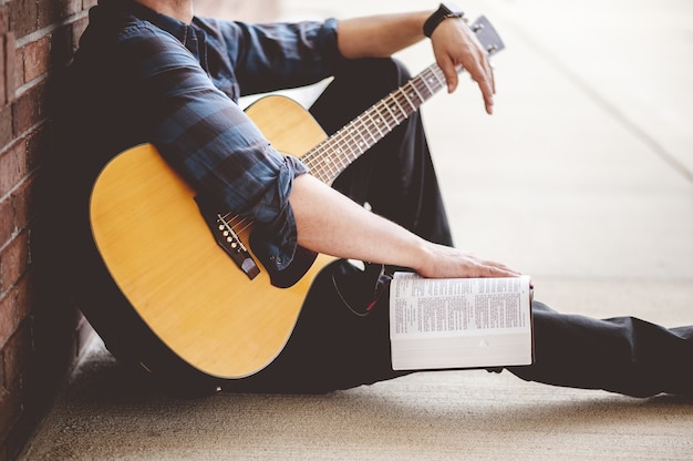 Primer plano de un hombre joven sentado con un libro y una guitarra en las manos