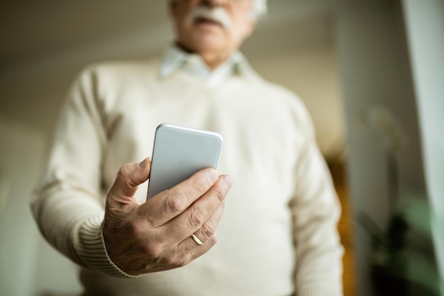 Primer plano de un hombre maduro usando un teléfono inteligente en casa