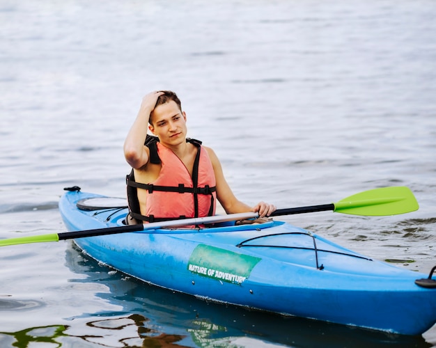 Primer plano de hombre con la mano en la cabeza con remo flotando en kayak