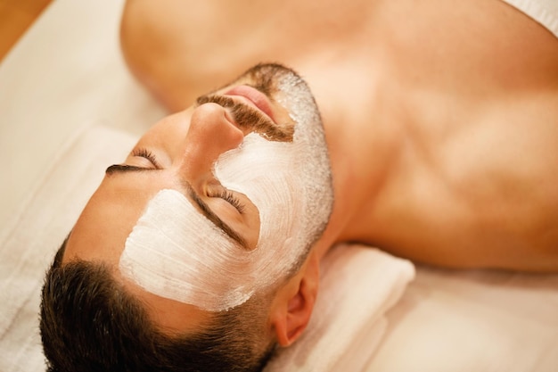 Foto gratuita primer plano de hombre con máscara facial blanca relajante durante el tratamiento en el spa de belleza