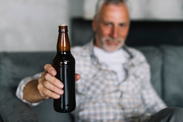 Primer plano de un hombre mayor que muestra la botella de cerveza con espuma