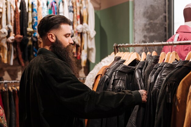 Primer plano de un hombre mirando la chaqueta de cuero en el carril en la tienda de ropa