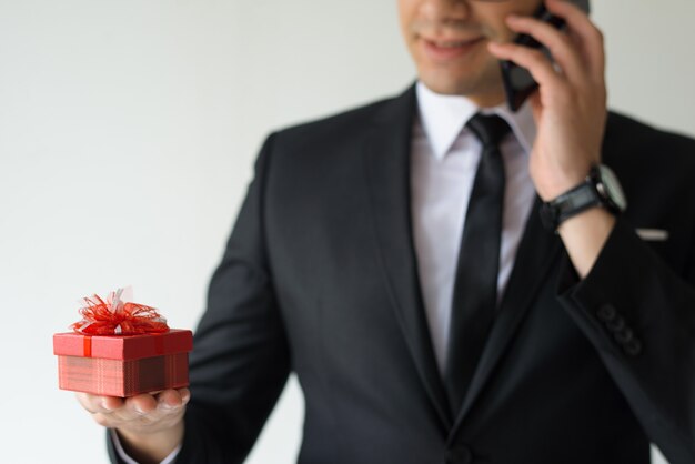 Primer plano de hombre de negocios con caja de regalo y hablando por teléfono