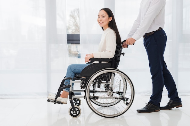 Foto gratuita primer plano de un hombre de negocios empujando a la mujer con discapacidad sentada en silla de ruedas