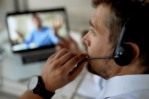 Primer plano de un hombre de negocios hablando en línea con su colega mientras usa una computadora portátil en la oficina