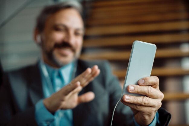 Primer plano de un hombre de negocios que usa un teléfono móvil para una videollamada desde la oficina