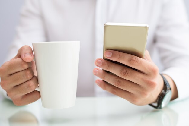 Primer plano de hombre de negocios tomando café y usando teléfono inteligente