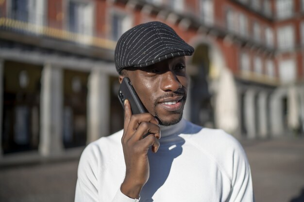 Primer plano de un hombre negro con sombrero y cuello alto hablando por teléfono