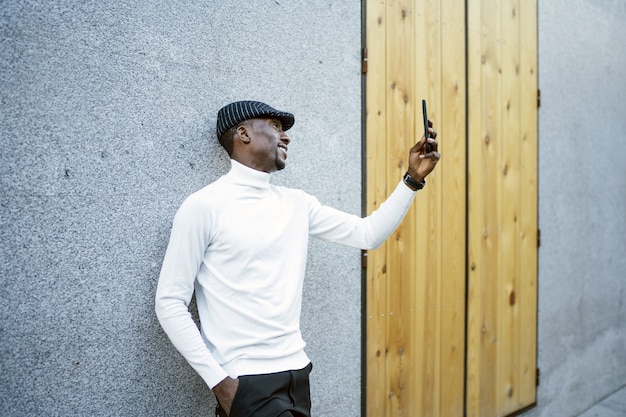 Primer plano de un hombre negro con sombrero y cuello alto tomando un selfie