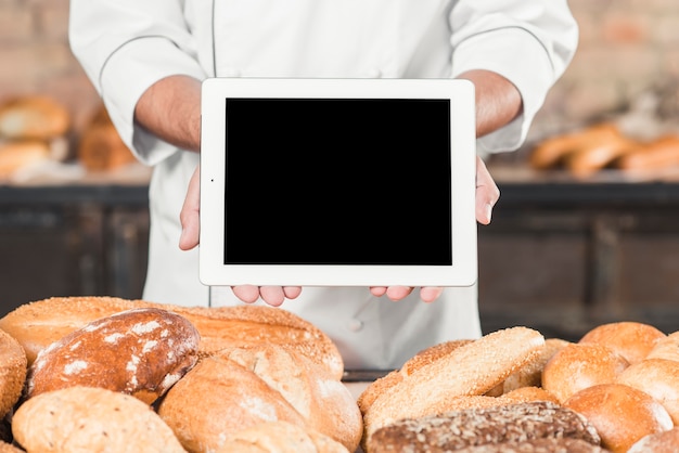 Primer plano de hombre panadero mostrando tableta digital en blanco sobre el pan horneado