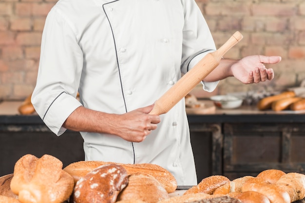 Primer plano de hombre panadero de pie detrás de la mesa con rodillo