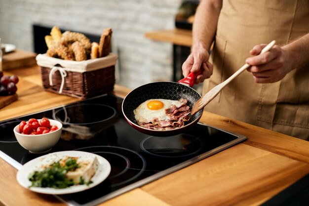 Primer plano de hombre preparando huevos de amigo con tocino en la cocina