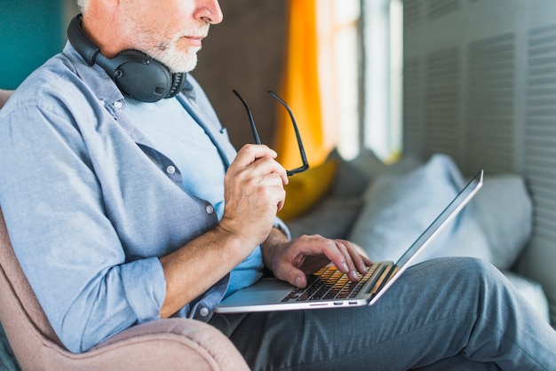 Primer plano, de, hombre que sostiene, anteojos, usar la computadora portátil