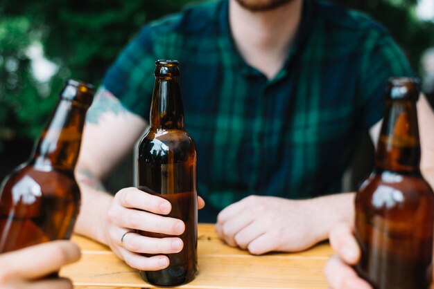 Primer plano de un hombre que sostiene la botella de cerveza marrón con sus amigos