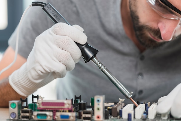 Primer plano de un hombre que suelda el circuito de computadora en taller