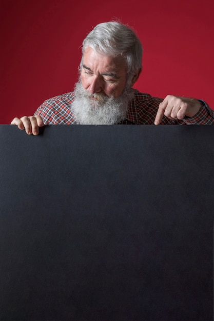 Primer plano de hombre senior con barba gris apuntando su dedo en cartel negro en blanco