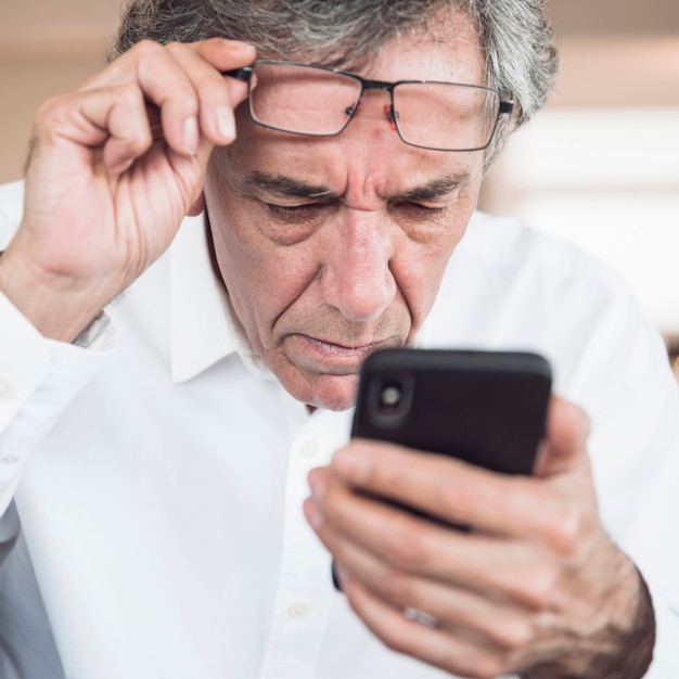 Primer plano de hombre senior serio mirando teléfono inteligente