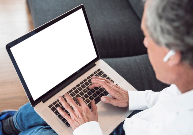 Primer plano de hombre senior usando laptop con pantalla blanca