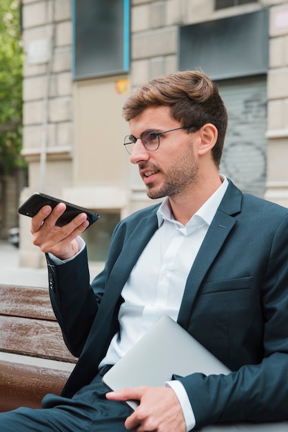 Primer plano de un hombre sentado en un banco hablando por teléfono con el asistente de voz digital