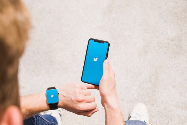 Primer plano de hombre con smartwatch y teléfono móvil que muestra la aplicación de twitter