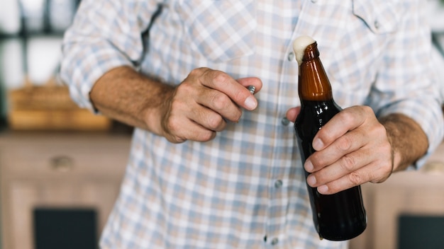 Primer plano de hombre sosteniendo una botella de cerveza abriéndose con espuma