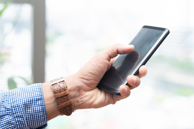 Primer plano de hombre sosteniendo teléfono inteligente y tocando en su pantalla