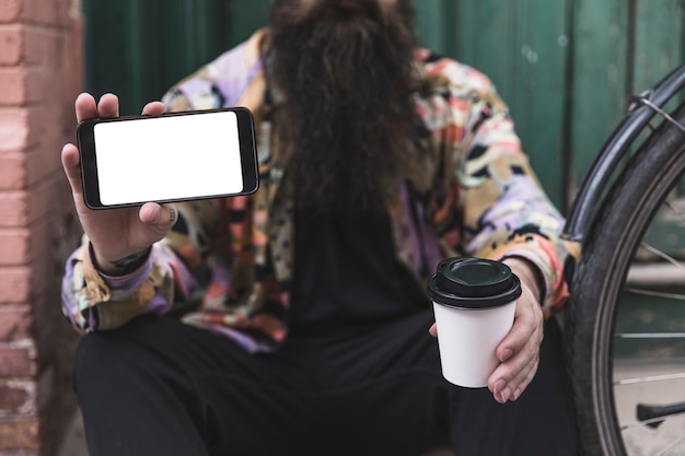 Foto gratuita primer plano de un hombre sosteniendo un teléfono móvil y una taza de café desechable en la mano