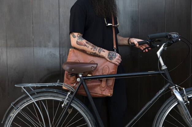 Primer plano de un hombre con su bolsa y bicicleta frente a una pared negra