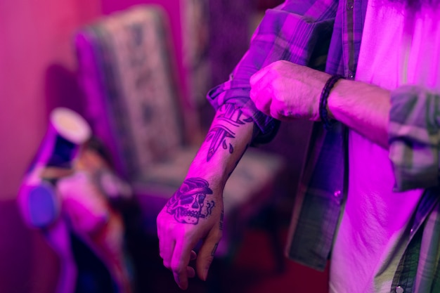 Primer plano de un hombre con un tatuaje en la mano doblando las mangas de la camisa