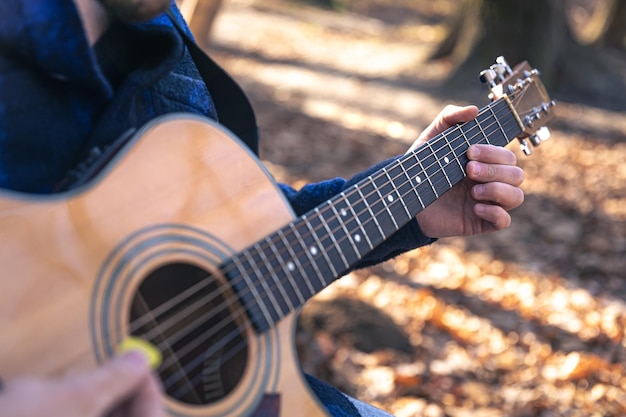 Foto gratuita primer plano un hombre toca una guitarra acústica en el bosque de otoño