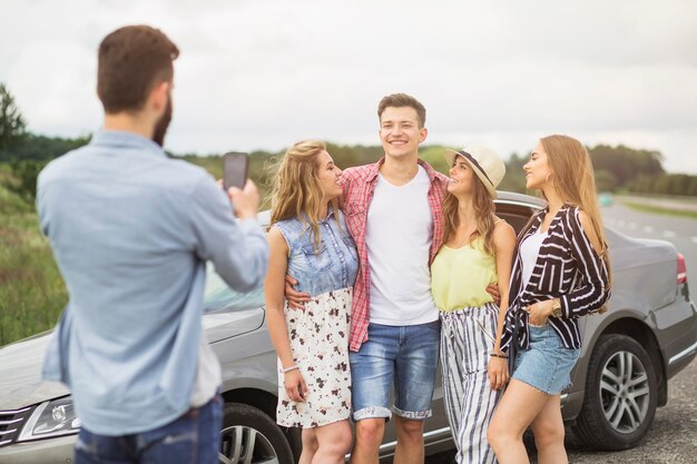 Primer plano de hombre tomando fotos de amigos de pie cerca del coche