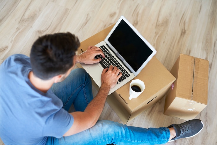 Foto gratuito un primer plano de un hombre usando una computadora portátil junto a cajas en movimiento