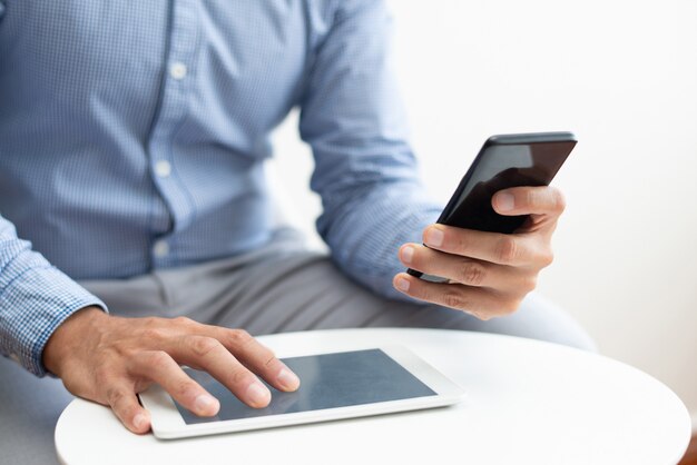 Primer plano de hombre usando teléfono inteligente y tableta en mesa de café