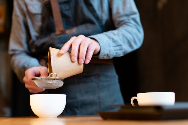Primer plano del hombre vertiendo café en taza a través del tamiz