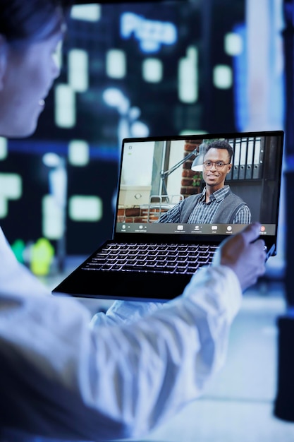 Foto gratuita primer plano de un hombre en videollamada con un compañero de trabajo mientras camina por las avenidas de la ciudad por la noche, brindándole actualizaciones sobre su trabajo. la persona usa una computadora portátil para mostrarle a su colega el paisaje urbano de la vida nocturna en un fondo borroso