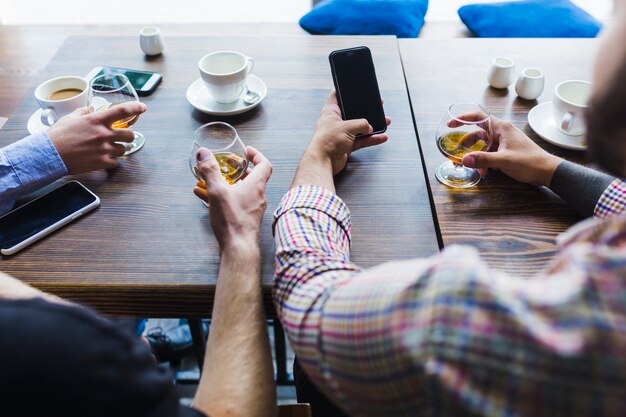 Primer plano de hombres mano vasos de bebidas con teléfono móvil