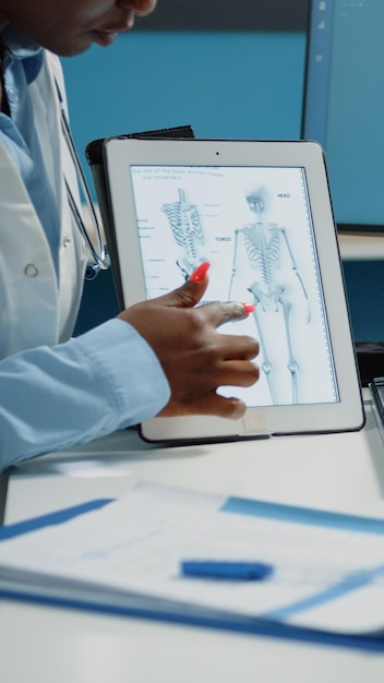 Primer plano de la imagen del esqueleto humano en la tableta para el examen de osteopatía en el consultorio médico. Dispositivo de sujeción del médico con anatomía ósea para el diagnóstico de osteoporosis y el tratamiento de la salud.