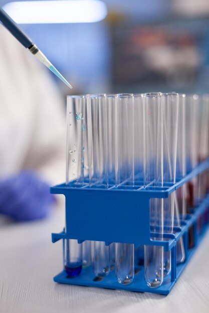 Primer plano de un investigador especializado que pone la solución en tubos de ensayo transparentes que trabajan en el desarrollo de vacunas durante el experimento microbiológico. Laboratorio de microbiología con equipamiento médico.