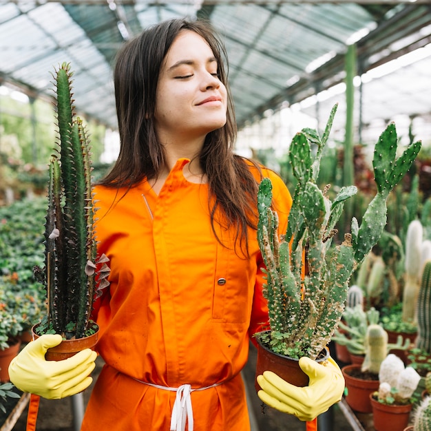 Primer plano de un jardinero de sexo femenino joven que sostiene las plantas en maceta del cactus