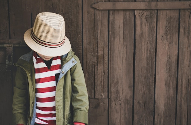 Foto gratuita primer plano de un joven con un abrigo verde, camisa a rayas y un sombrero sobre un fondo de madera