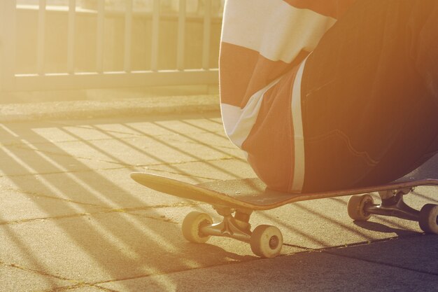 Primer plano de joven adolescente tener descanso o sentarse en un parque de patinaje en día de verano al aire libre, vista lateral. Área urbana. Viraje.