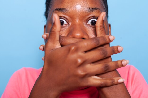 Primer plano de una joven afroamericana que cubre la boca habiendo conmocionado expresiones faciales